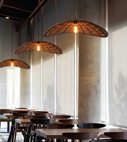 Three woven wicker pendant lights with warm glowing bulbs hanging over a dining area with wooden tables and chairs.