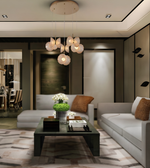 A modern living room interior featuring a multi-light pendant chandelier with white flower-shaped glass shades hanging over a dark coffee table, flanked by light gray sofas with brown accent pillows.