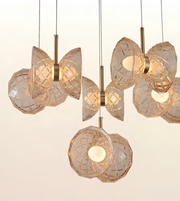 A modern multi-light pendant chandelier with faceted clear glass shades and warm brass-toned metal hardware, shown hanging against a plain light background.