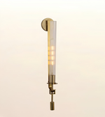 A modern wall-mounted light fixture with a vertical frosted glass shade and warm brass-toned metal hardware, shown against a plain light background.