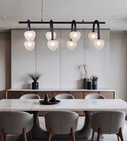 Modern dining room featuring a black linear ceiling light fixture with six curved arms and glowing white glass globes, above a white marble dining table with gray upholstered chairs.