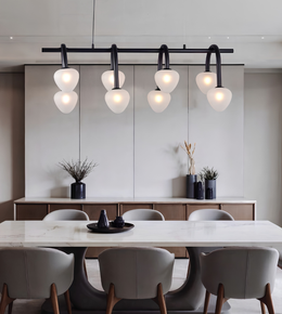 Modern dining room featuring a black linear ceiling light fixture with six curved arms and glowing white glass globes, above a white marble dining table with gray upholstered chairs.