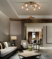 A modern living room interior featuring a decorative ceiling light fixture with multiple warm glowing bulbs and flower-like shades, along with a sofa, armchair, coffee table, and dining area in the background.