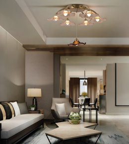 A modern living room interior featuring a decorative ceiling light fixture with multiple warm glowing bulbs and flower-like shades, along with a sofa, armchair, coffee table, and dining area in the background.