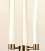 A close-up of a modern three-light fixture with vertical ribbed glass tubes and a brushed brass-finished metal base and arm connectors, set against a warm off-white background.