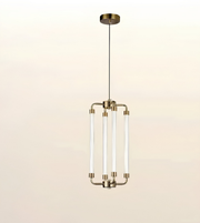 A modern multi-light linear pendant chandelier with four clear glass tubes and brushed brass hardware, suspended against a light beige gradient background.