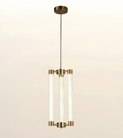A modern three-light linear pendant chandelier with clear glass cylindrical tubes and brushed brass hardware, suspended from a round ceiling canopy against a light beige background.