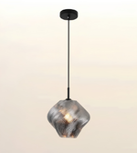A modern pendant light with a textured, ribbed glass shade in a metallic silver finish, suspended by a slim black cord from a matching black ceiling canopy against a soft, light beige gradient background.