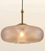 A modern pendant light with a textured, diamond-patterned glass shade in a warm champagne or blush tone, suspended by a brass-colored rod against a plain off-white background.