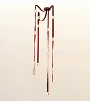 A hanging decorative wind chime with dark reddish-brown ribbons and cream circular beads, suspended from a dark metal fixture against a plain light background.