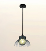A modern pendant light with a black ceiling canopy and cord, featuring a textured clear glass shade with layered petal-like rings around a glowing warm bulb.