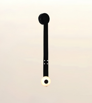 A minimalist black wall sconce with a circular black backplate and a spherical white globe shade featuring a black center, shown against a soft beige gradient background.