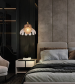 A modern bedroom interior featuring a bed with light gray bedding, a matching upholstered headboard, a black slatted accent wall, a pendant lamp with a white flower-like shade and warm glowing bulb, and a small white nightstand.