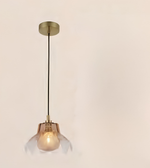 A modern pendant light with a round brass ceiling canopy, a thin black cord, and a bell-shaped clear glass shade that glows with a warm light from the visible bulb inside.