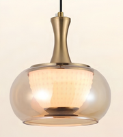 A modern pendant light with a brushed brass-finished metal neck and a large, rounded clear glass shade that glows warm white with an internal textured diffuser.