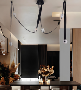 Modern multi-light pendant chandelier with black fabric cords, white circular diffusers, and spherical globe shades, shown hanging in a contemporary interior space.