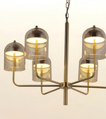 A modern six-light chandelier with a brushed brass metal frame and translucent smoky glass dome shades, shown against a plain off-white background.