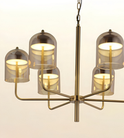 A modern six-light chandelier with a brushed brass metal frame and translucent smoky glass dome shades, shown against a plain off-white background.
