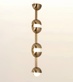 A modern vertical pendant light fixture with four elongated metallic gold spherical shades separated by horizontal white bars, shown against a soft beige gradient background.