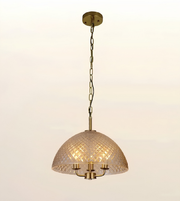 A dome-shaped pendant light with a textured, diamond-patterned glass shade and a brass-finished metal frame, hanging from a matching brass ceiling canopy and chain against a plain off-white background.