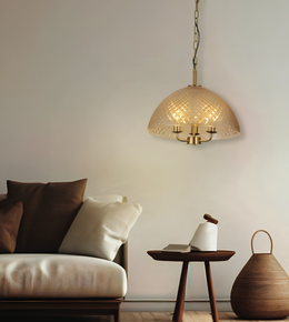 A warm brass pendant light with a textured, diamond-patterned glass dome shade hangs above a small wooden side table in a modern, minimalist living room setting.