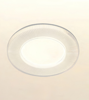 A modern circular flush-mount ceiling light with a ribbed clear acrylic outer ring and a bright white illuminated center, shown against a plain off-white ceiling.