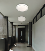 Two round flush-mount ceiling light fixtures installed on a white ceiling in a modern hallway with gray tiled walls and a dark wooden door.