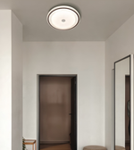A modern circular flush-mount ceiling light with a white frosted center and a black outer rim, installed on a white ceiling in a minimalist hallway.