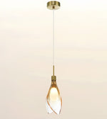 A modern single pendant light with a brushed brass ceiling canopy, cord, and cap, featuring a clear glass shade with twisted spiral edges that glow warm yellow from the light bulb inside.