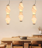Three modern pendant lights with sculptural, ribbed paper lantern-style shades hanging above a wooden dining table in a warm, minimalist interior.