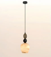 A modern pendant light with a black metal canopy and cord, featuring a smoky glass decorative bead, a black sphere accent, and a warm marbled amber glass shade, shown against a soft beige gradient background.