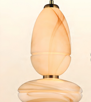 A close-up of a sculptural pendant light with a warm, glowing marbled glass shade in cream and amber tones, featuring a brass-toned metal top and bottom.