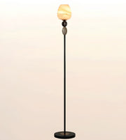 A modern floor lamp with a slim black metal stand, a round black base, and a sculptural marbled cream and orange glass shade at the top, shown against a soft beige gradient background.