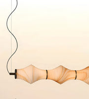 A modern pendant light with a ribbed, translucent beige shade that glows warm white, suspended by a black cord against a pale cream background.