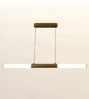 A modern linear pendant light fixture with a horizontal bar, featuring a brushed brass or bronze metal frame and a glowing white frosted glass tube. It hangs from a matching rectangular ceiling canopy with two thin suspension wires, set against a plain off-white background.