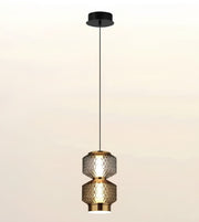 A modern pendant light fixture with two stacked textured glass shades in a warm metallic finish, suspended by a slim black cord from a matching black ceiling canopy against a soft beige gradient background.