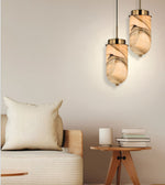 Two modern pendant lights with beige and brown marbled glass shades hanging above a sofa in a styled living room setting.