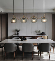A modern dining room featuring a white marble dining table surrounded by gray upholstered chairs, under four textured glass pendant lights with gold-toned zigzag metal frames.