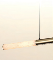 A modern linear pendant light with a cylindrical frosted glass shade and a brushed brass metal tube, suspended by a thin black cord against a plain off-white background.