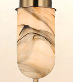 A modern pendant light fixture with a cylindrical glass shade featuring a warm beige, cream, and brown marbled swirl pattern, finished with brushed brass metal hardware at the top and bottom.
