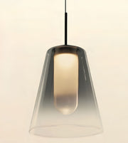 A modern pendant light with a tapered clear glass shade and a black hanging cord, shown against a plain light beige background.