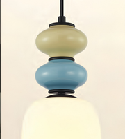 A modern pendant light fixture with a stacked, bubble-like design featuring a cream top section, a light blue middle section, and a glowing warm white bottom shade, suspended by a black rod.