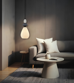 A modern pendant light with a glowing frosted glass shade hangs above a gray sofa in a minimalist living room setting with a round coffee table and neutral decor.