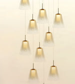 A modern multi-light pendant chandelier with nine clear glass bell-shaped shades suspended at varying heights against a warm off-white background.