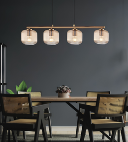 A modern 4-light linear pendant ceiling light with ribbed clear glass shades and a warm brass/gold-toned frame, hanging above a dining table with woven-back chairs in a dark gray room.