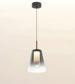 A modern pendant light with a tapered clear glass shade and a black ceiling canopy and cord, shown against a plain light beige background.