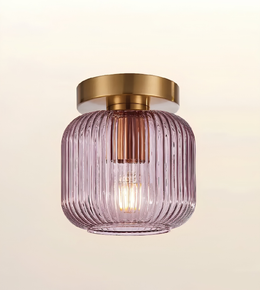 A modern semi-flush mount ceiling light featuring a ribbed, translucent lavender-purple glass shade and a brushed gold metal canopy, shown against a warm off-white background.