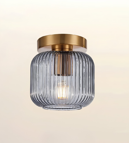 A modern semi-flush mount ceiling light fixture featuring a ribbed, translucent smoky gray glass shade and a brushed gold metal canopy, shown against a soft beige gradient background.