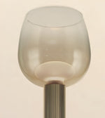 A close-up of a modern table lamp featuring a translucent frosted glass shade with a flared rim and a ribbed metallic stem in a warm brushed gold finish, set against a solid cream background.