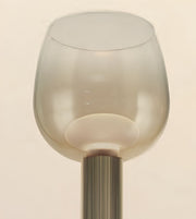 A close-up of a modern table lamp featuring a translucent frosted glass shade with a flared rim and a ribbed metallic stem in a warm brushed gold finish, set against a solid cream background.